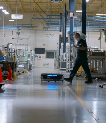 A worker walks with a robot on an assembly line, both engaged in the manufacturing process.